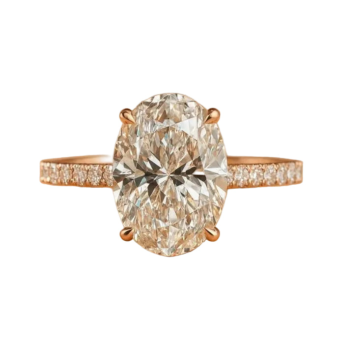 An oval diamond engagement ring with a rose gold band set with small pavé diamonds, centered on a warm tan background.