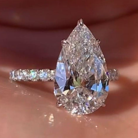 A pear-cut diamond ring with a pavé band, resting on a person's palm with fingers visible at the top.
